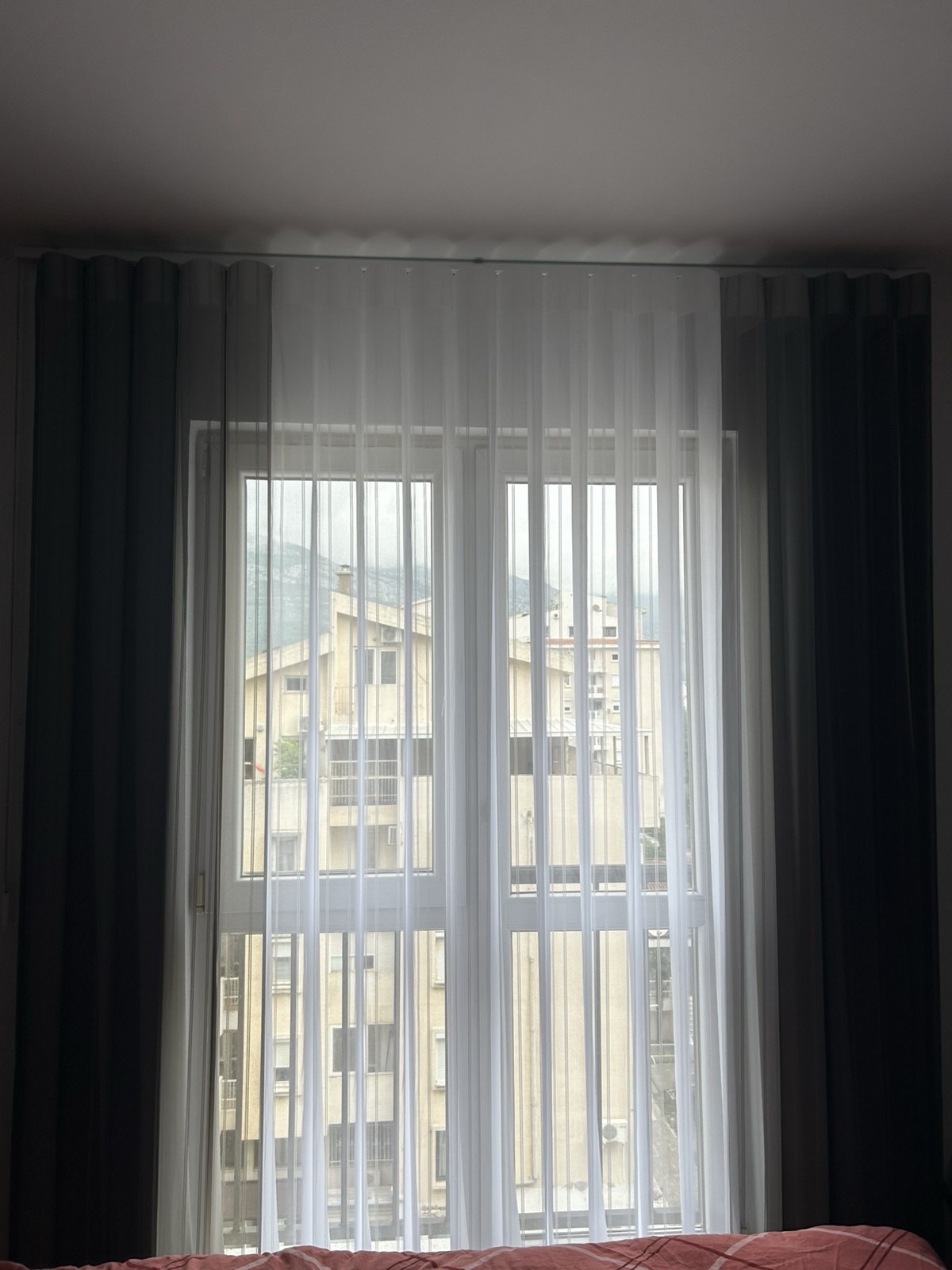 Dikey zavjese bijele i tamne tkanine u spavaćoj sobi, pogled na grad
